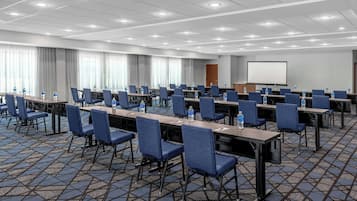 Una sala de conferencias con varias mesas, sillas y una pantalla de proyector.