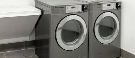 Zwei LG-Waschmaschinen für den gewerblichen Gebrauch in einem Waschraum mit weißer Arbeitsplatte und grauen Fliesenböden.