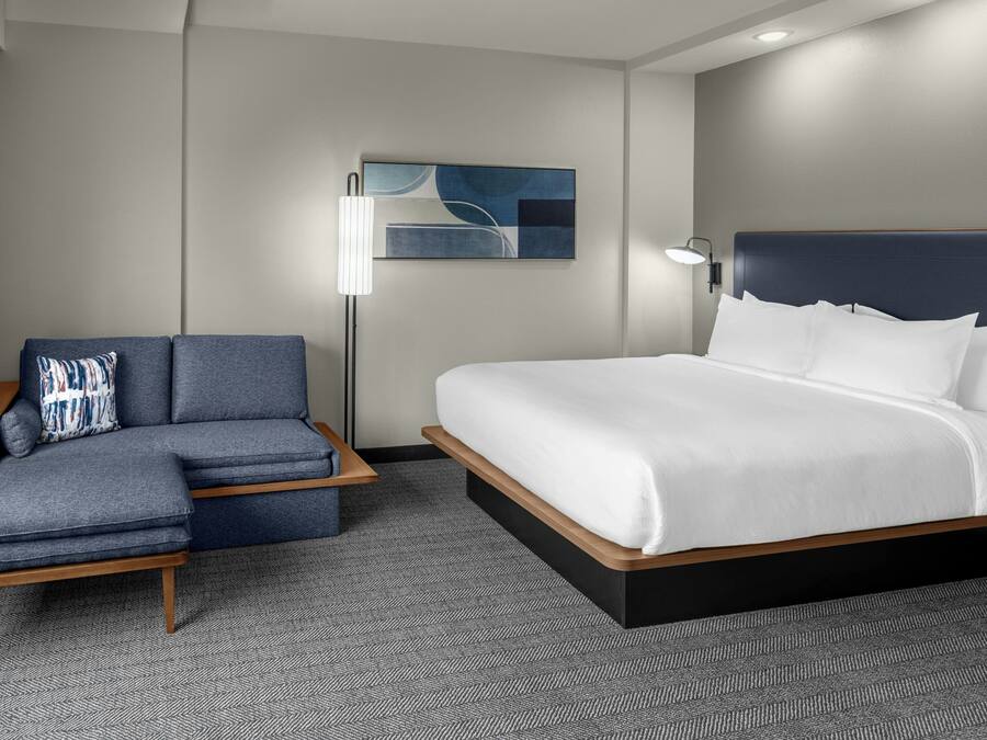 Una habitación de hotel moderna con cama, sofá, mesita auxiliar y lámpara.