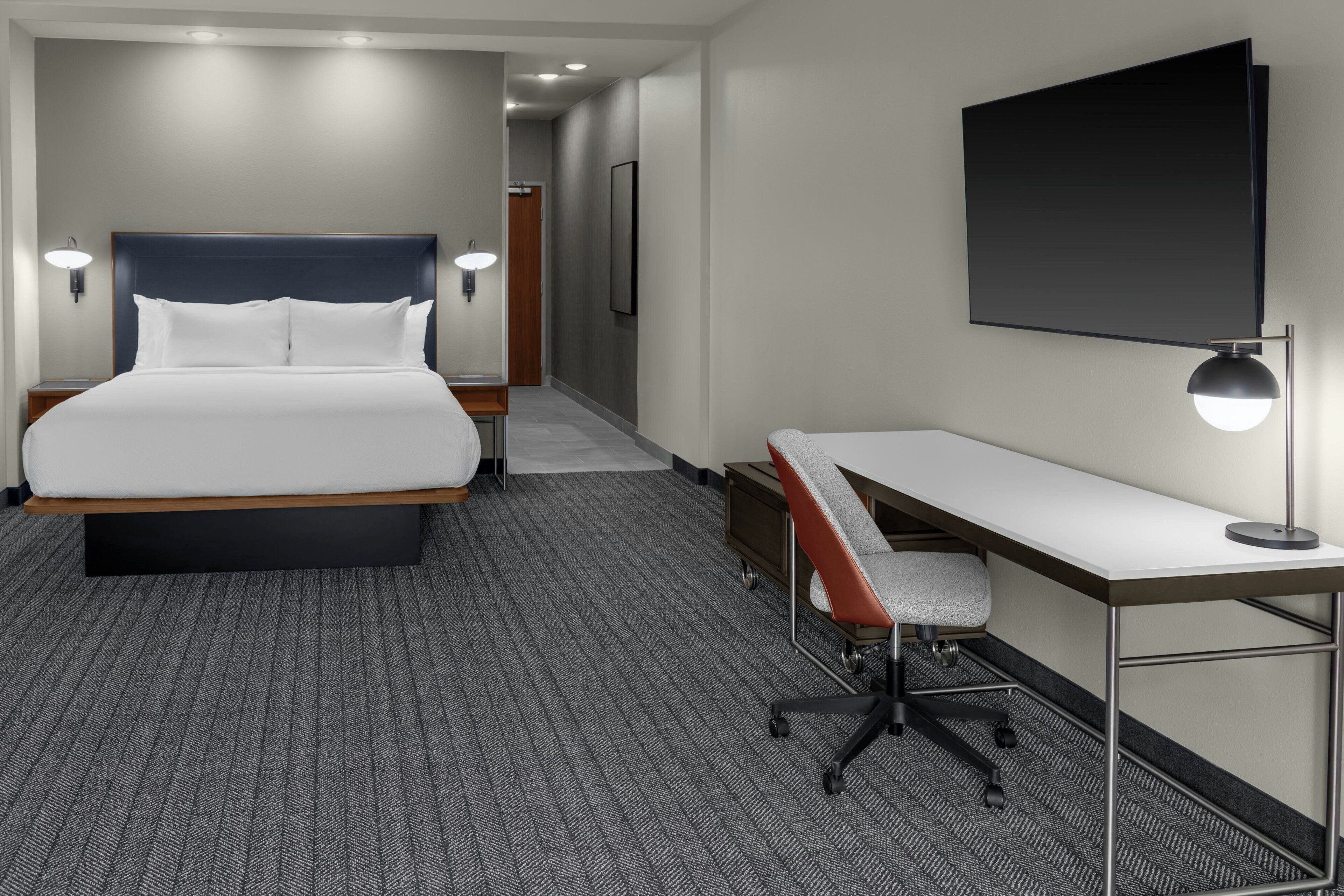 A hotel room with a bed, desk, chair, and a flat-screen TV.