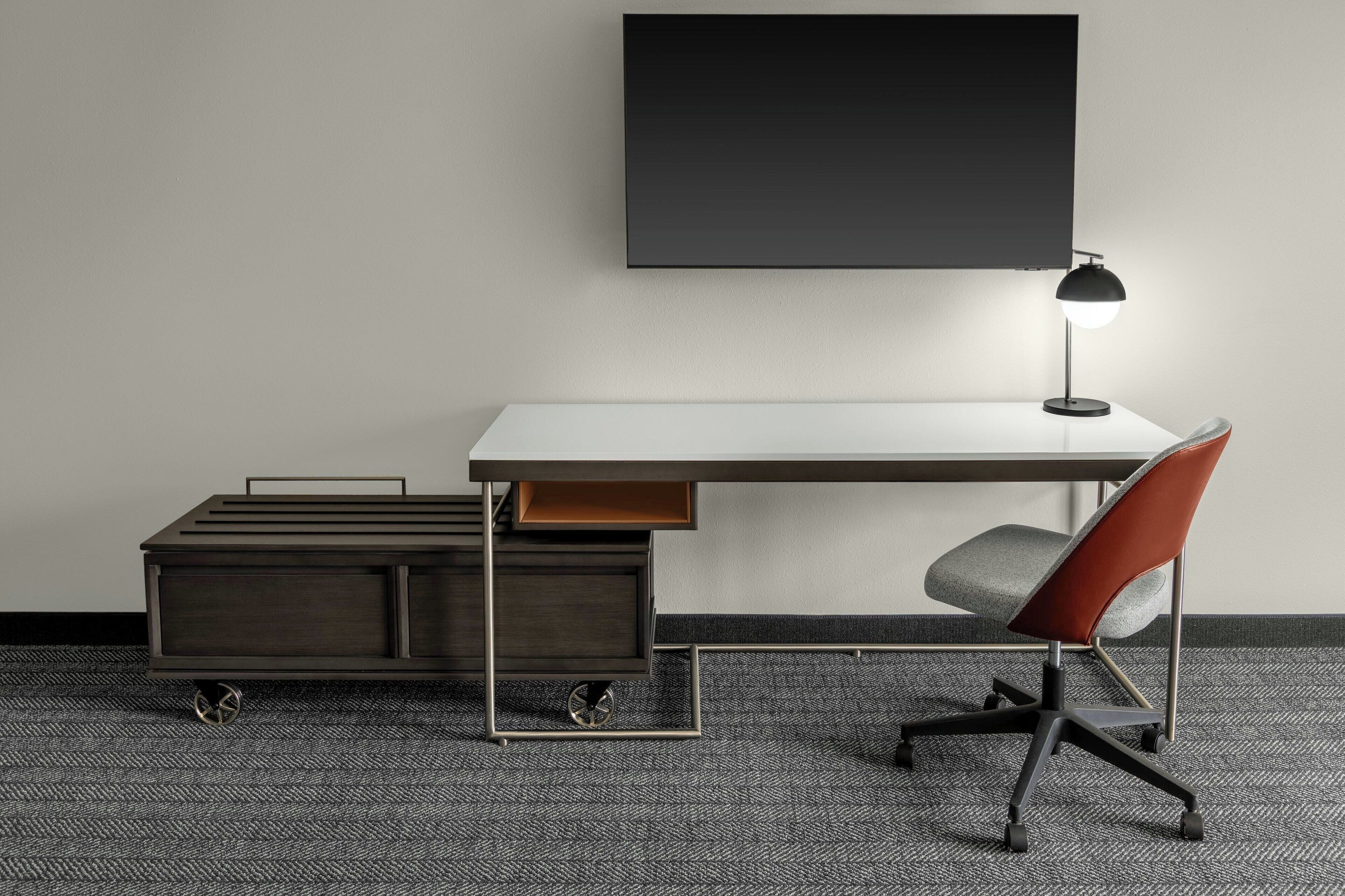 A modern office desk with a chair, a desk lamp, and a storage unit with wheels.