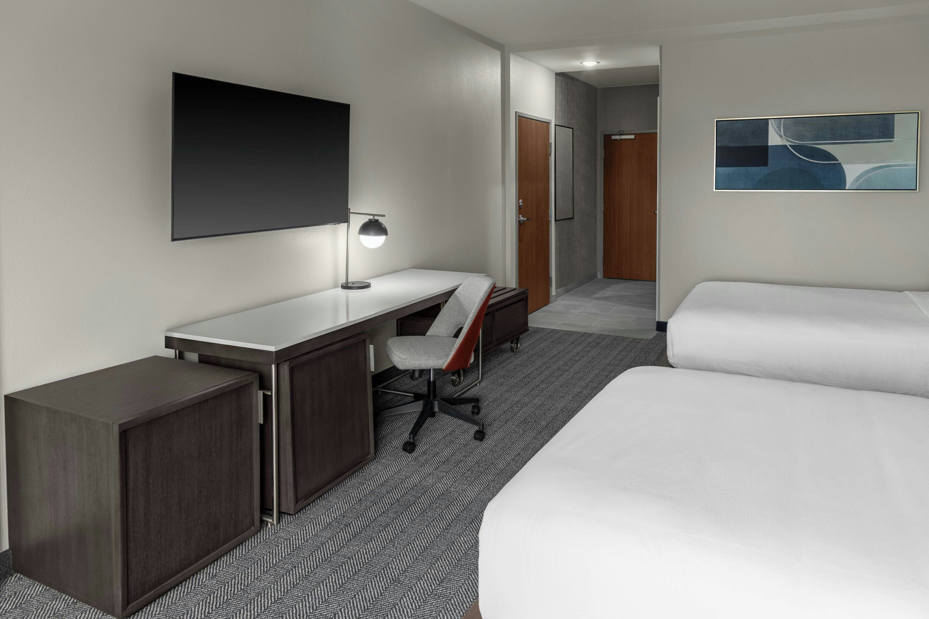 A hotel room with a desk, chair, and two beds.