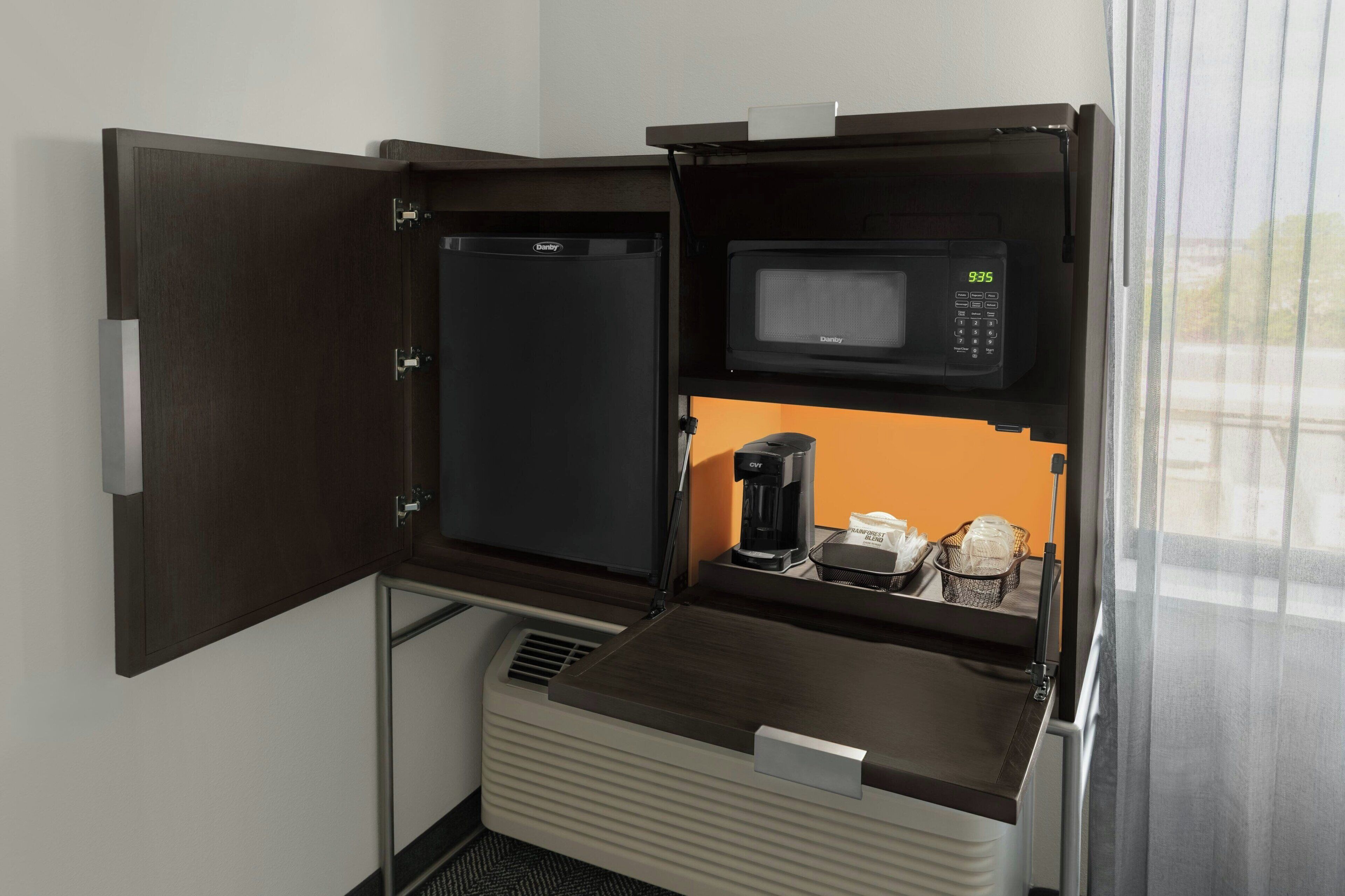 A compact kitchenette with a microwave, coffee maker, and storage space.