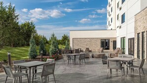 An outdoor patio area with multiple tables and chairs, surrounded by a stone-tiled floor, and a building with a stone facade in the background.