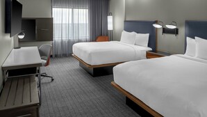 A hotel room with two beds, a desk, a chair, a TV, and a window with curtains.