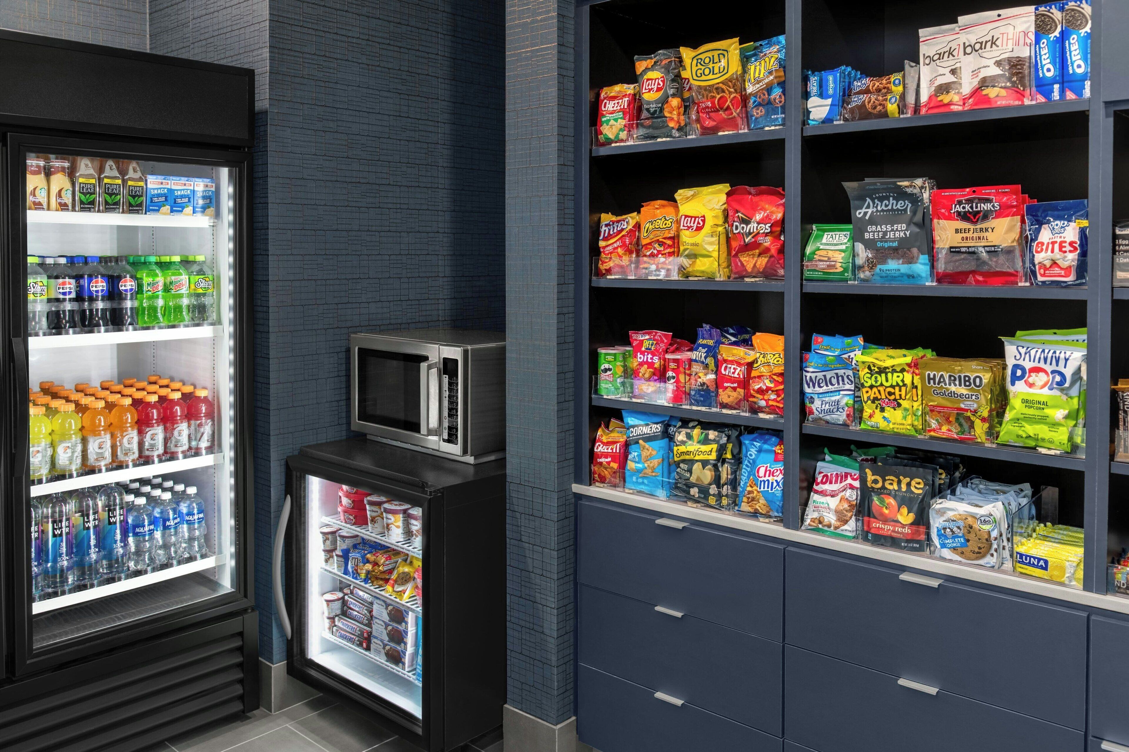 A snack and beverage refrigerator stocked with various drinks and snacks, including bottled water, sodas, and chips.