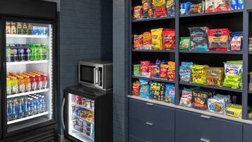 A snack and beverage refrigerator stocked with various drinks and snacks, including bottled water, sodas, and chips.