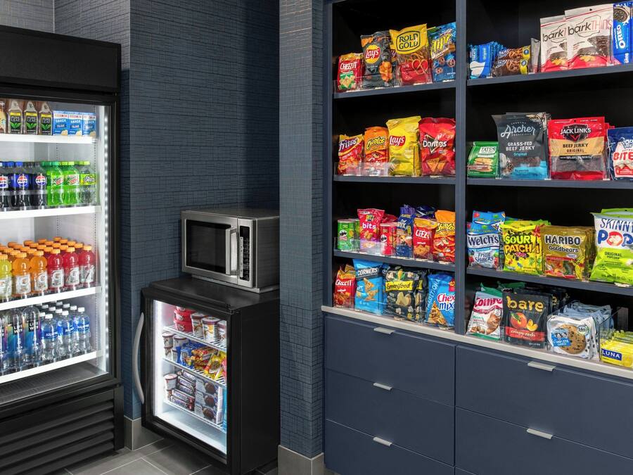 A snack and beverage refrigerator stocked with various drinks and snacks, including bottled water, sodas, and chips.