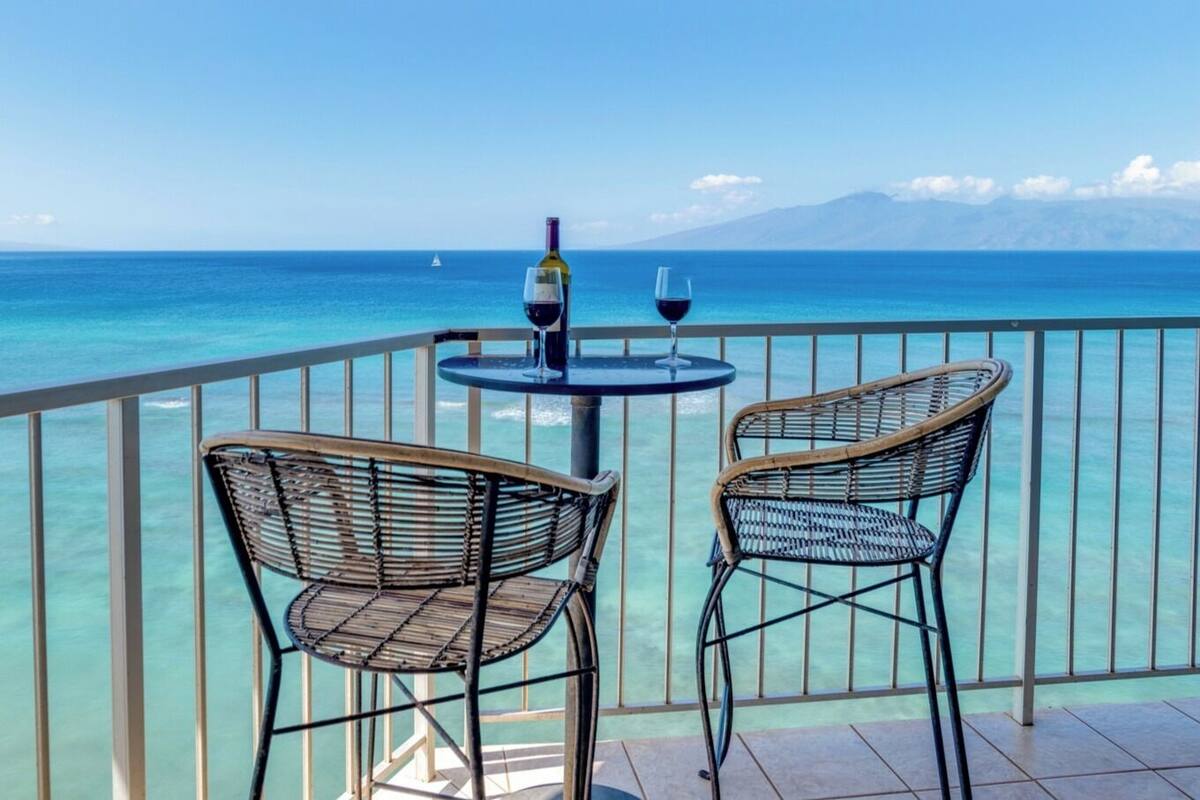 Ein Balkon mit zwei Korbstühlen und einem kleinen runden Tisch, jeweils mit einem Weinglas und einer Flasche Wein.