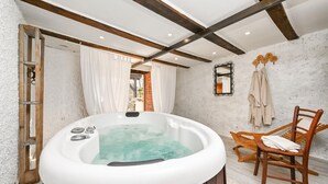 A bathroom with a hot tub, wooden beams, a wooden chair, and a mirror on the wall.