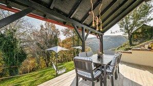 An outdoor patio with a table and chairs, surrounded by a garden and a view of hills.