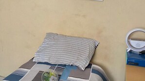 Una cama con almohadas a rayas, un reloj pequeño y un espejo en la pared.