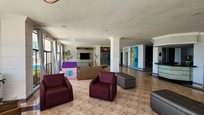 En rummelig lobby med reception, siddeområde med lænestole og sofa, samt et lille legeværelse.