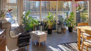 Habitación iluminada por el sol con vista a árboles, un sofá blanco, una mesita pequeña y varias plantas en macetas.