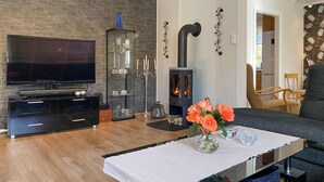 Una sala moderna con un televisor de pantalla plana, un mueble multimedia negro, una vitrina de vidrio, una estufa de leña negra y una mesa de comedor con un jarrón de flores.