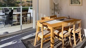 Comedor con una mesa y sillas de madera, una lámpara de araña y vistas al exterior a través de grandes ventanales.
