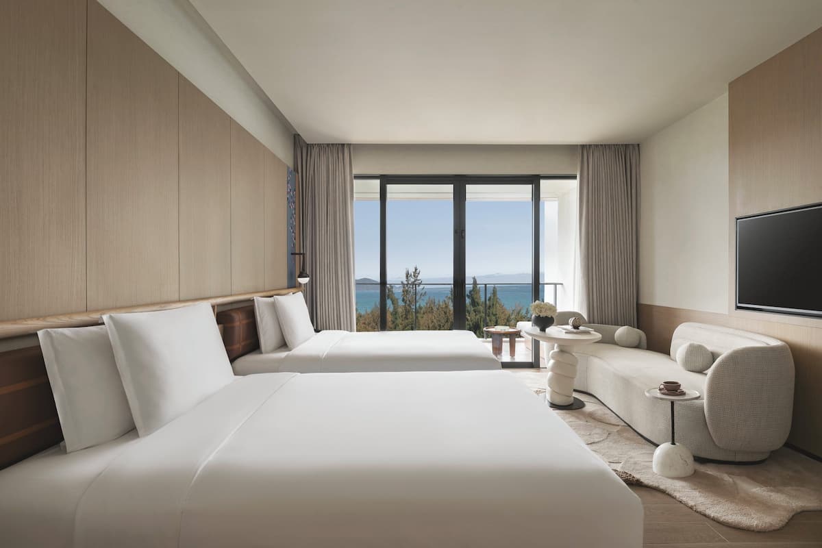 Habitació d'hotel amb dos llits grans, un sofà, una televisió i vista al mar.