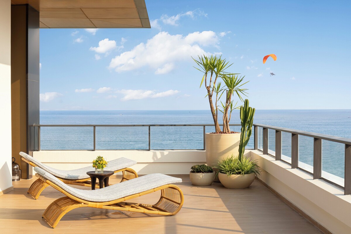 A balcony with wicker lounge chairs, a small table, and potted plants.