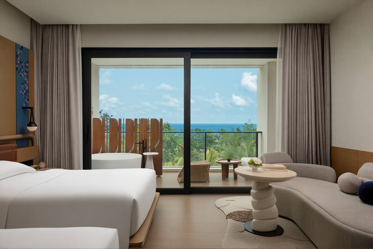 A hotel room with a large balcony, a bed, a sofa, and a small table.