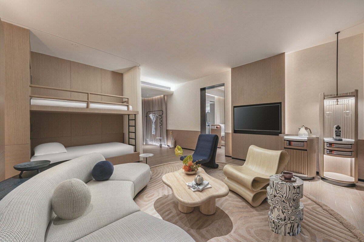 Una habitación de hotel moderna con sofá, sillón, mesita de café y televisor.