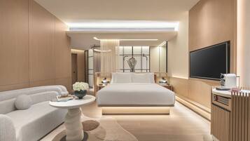 A modern hotel room with a large bed, a sofa, a small round table, and a TV mounted on the wall.