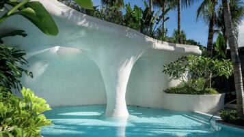 Ein Pool mit außergewöhnlichem architektonischen Design, umgeben von üppiger Vegetation und Palmen.
