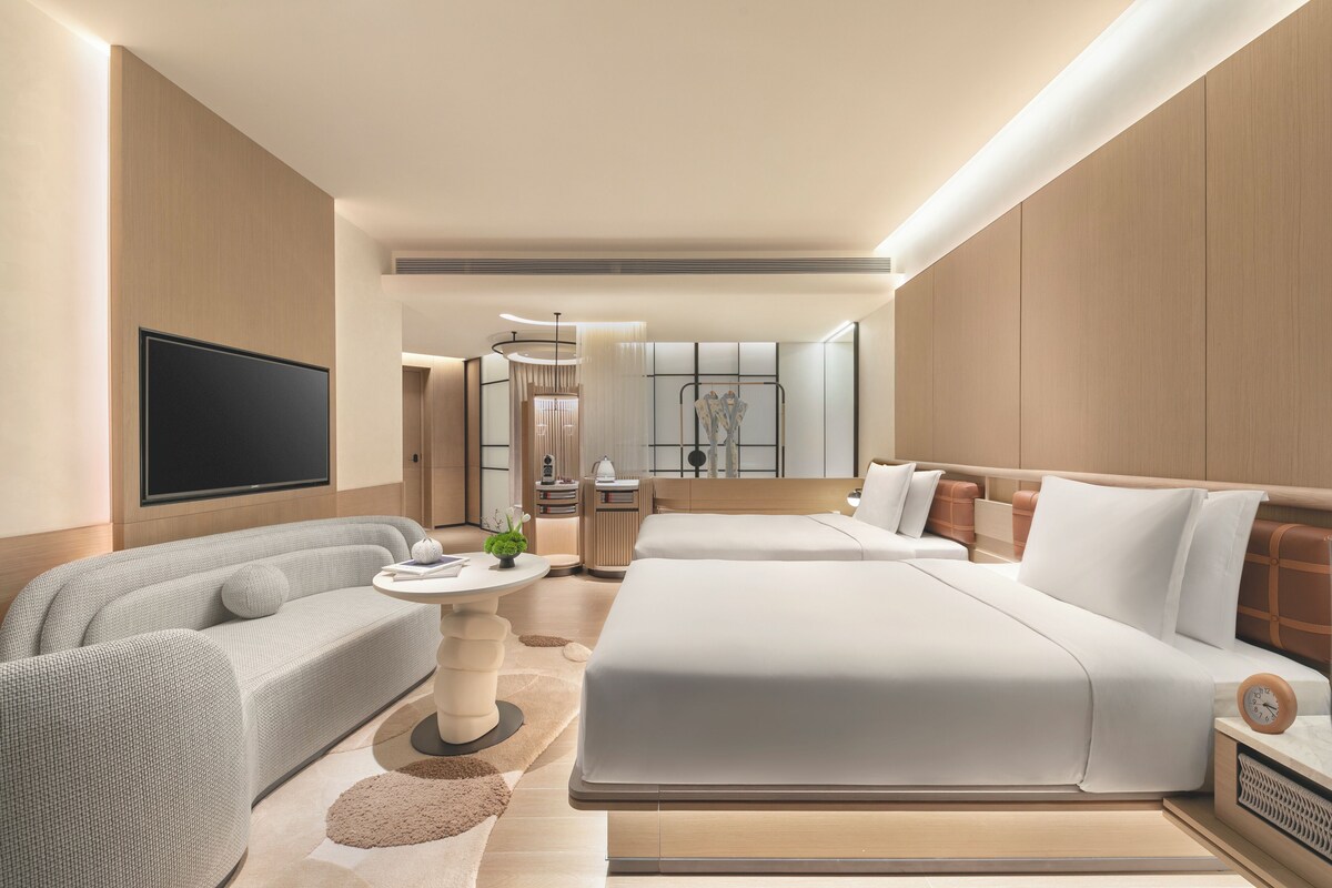 A modern hotel room with a large bed, a sofa, a TV, and a small table with a plant.