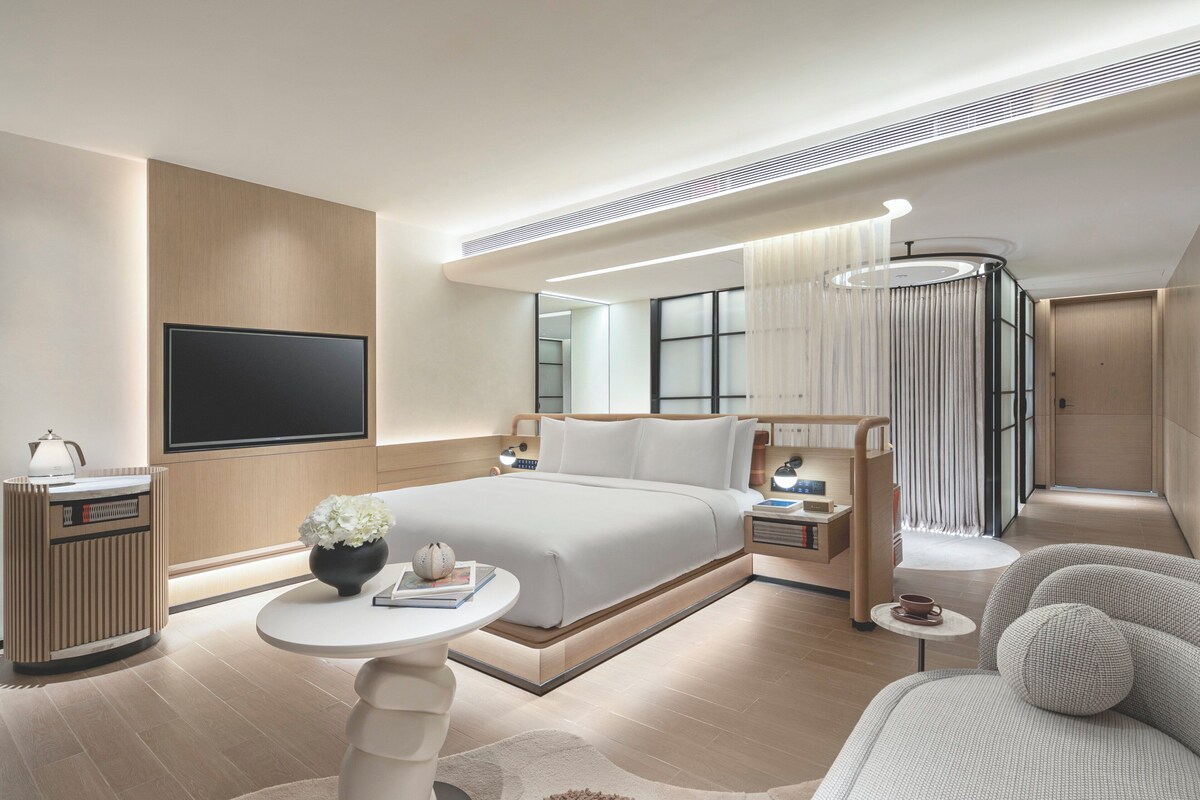 Una habitación de hotel moderna con una cama grande, un escritorio, un televisor y una zona de estar.