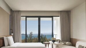 A hotel room with a large bed, a small table with a vase, a sofa, and a view of the sea through floor-to-ceiling windows. - Hotel Indigo Hainan Clear Water Bay by IHG (Lingshui)