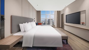 Una habitació d'hotel moderna amb un llit gran, una televisió penjada a la paret i vista a la ciutat per la finestra.