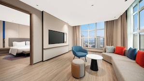 Habitació d'hotel moderna amb un llit gran, un sofà, un butàc blau, una taula de centre rodona i un televisor fixat a la paret.