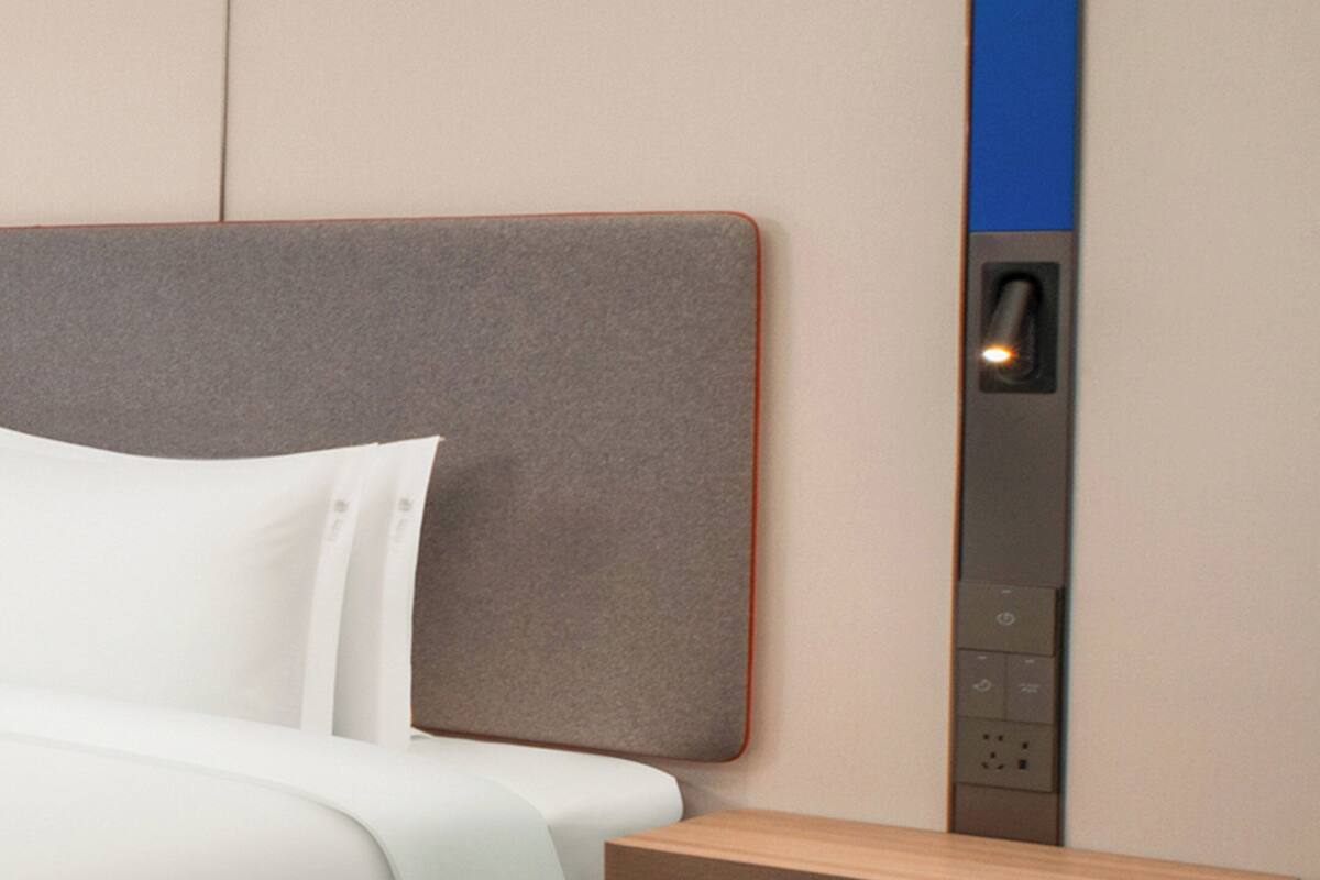 A modern hotel room with a bed, a headboard, and a control panel for room amenities.