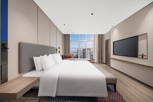 Habitación de hotel moderna con una cama grande, televisor, vistas a la ciudad y un escritorio.