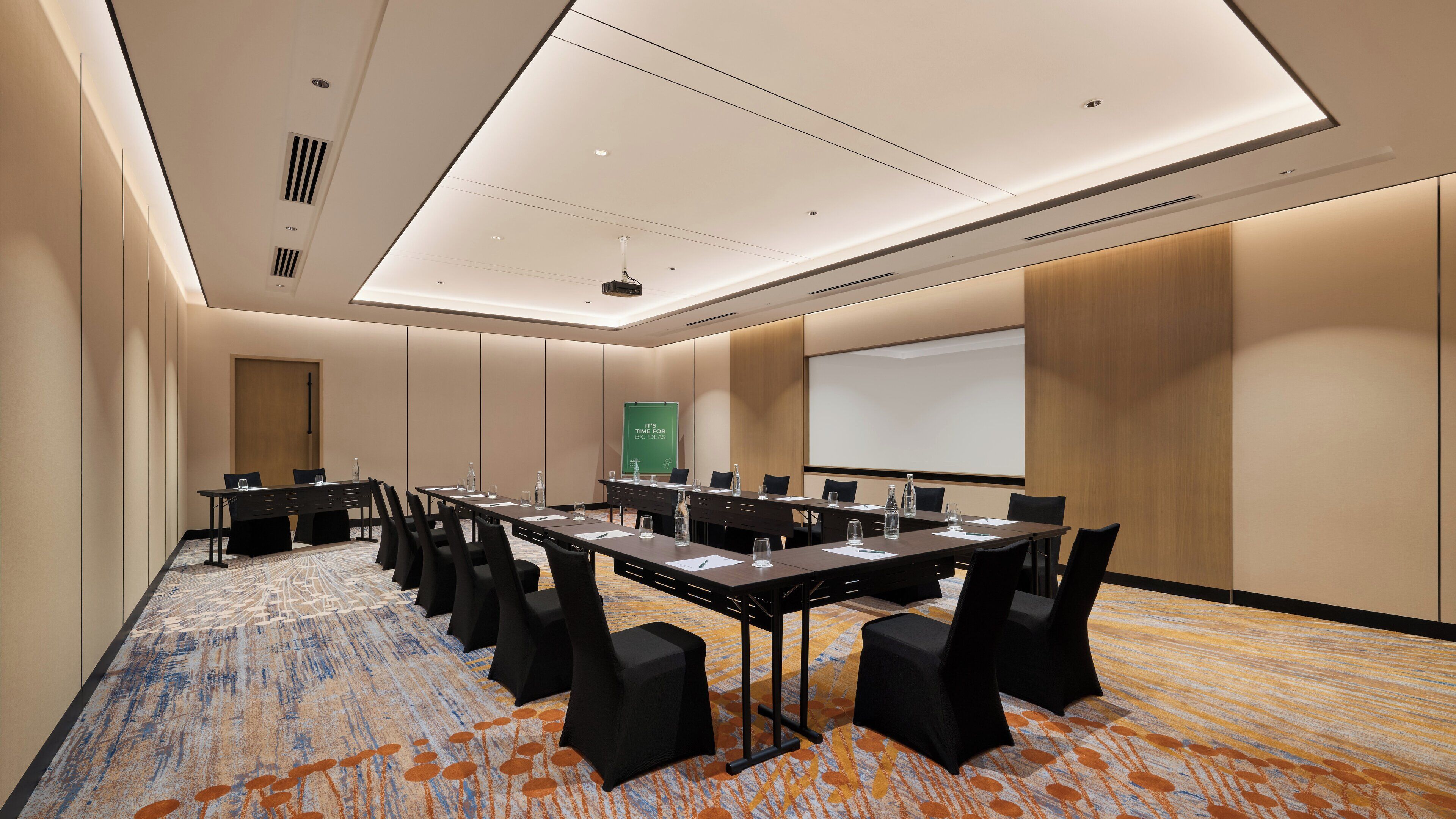 A conference room with a long table, chairs, a projector screen, and a presentation screen.