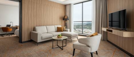 Una habitación de hotel moderna con sofá, sillón y televisor montado en la pared.