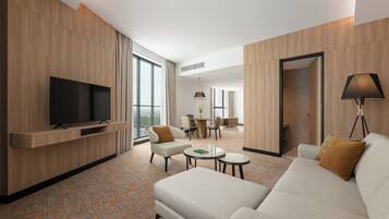 A modern hotel room with a flat-screen TV, a sofa, a dining area, and a large window offering a city view.