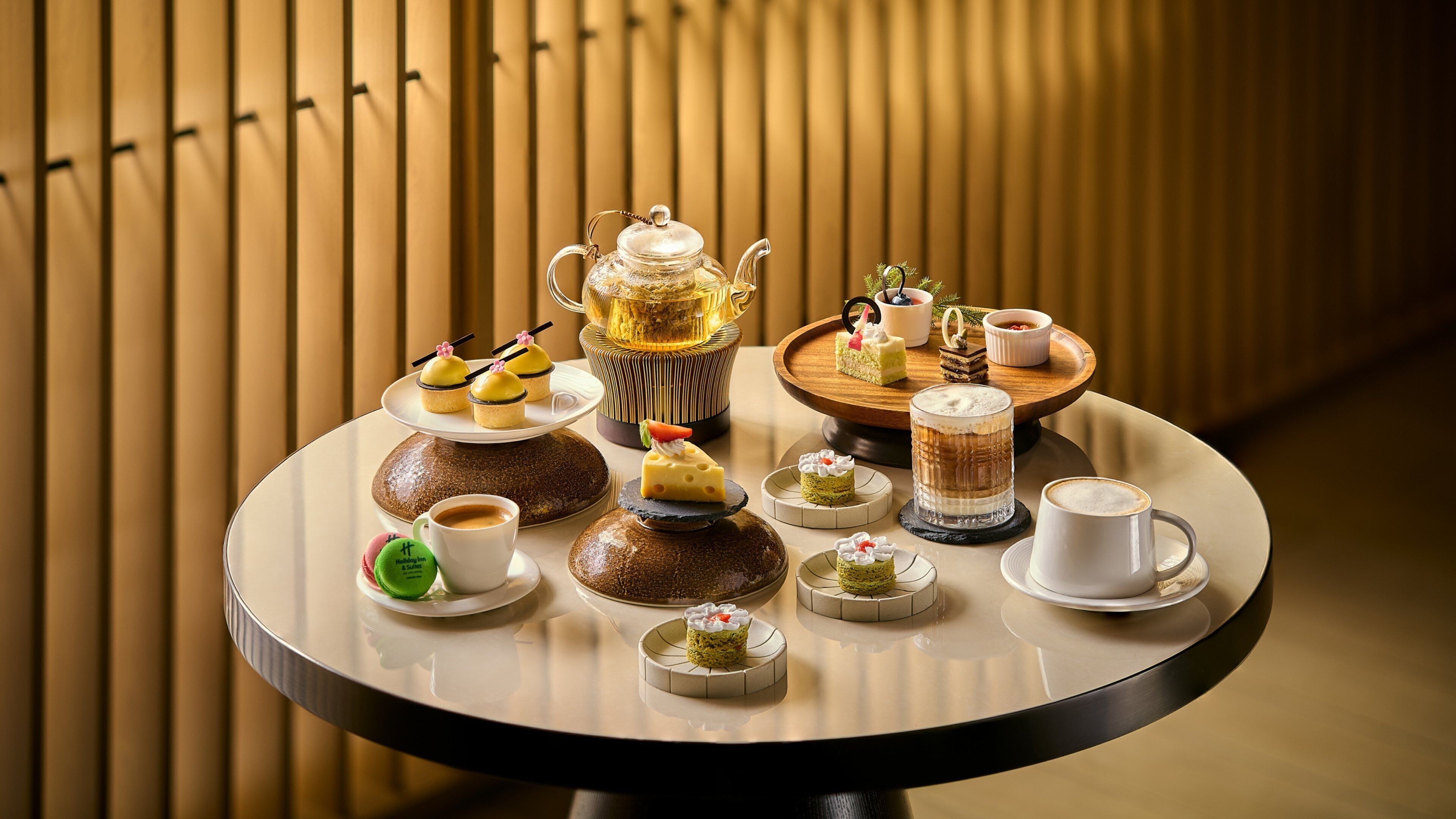 A round table with a variety of desserts, a teapot, and cups of coffee.
