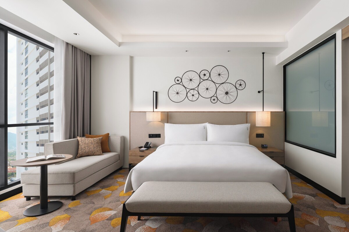 A modern hotel room with a large bed, a sofa, a small table, and a wardrobe.