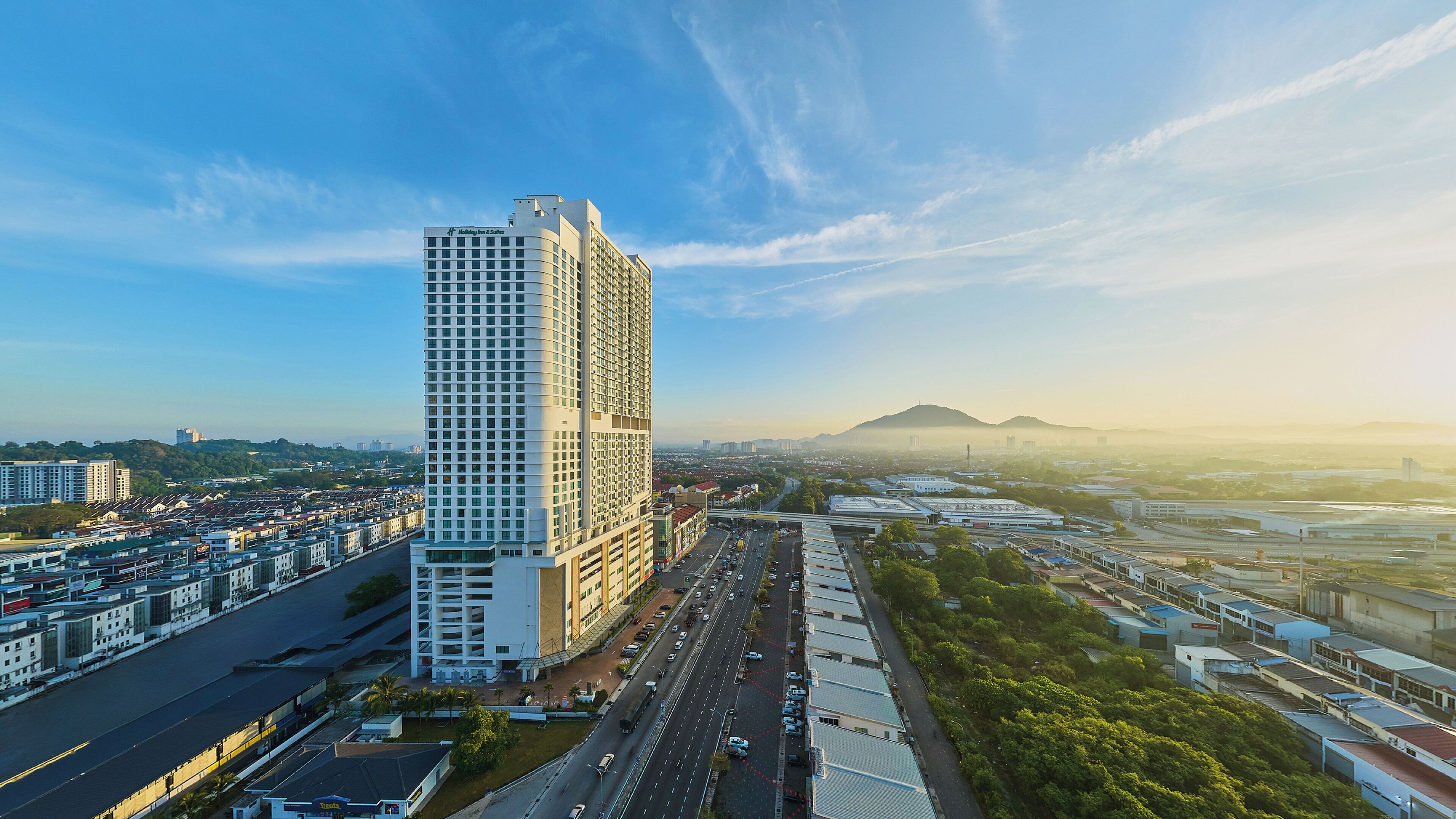 A high-rise hotel with a modern design, located near a busy road and surrounded by greenery.