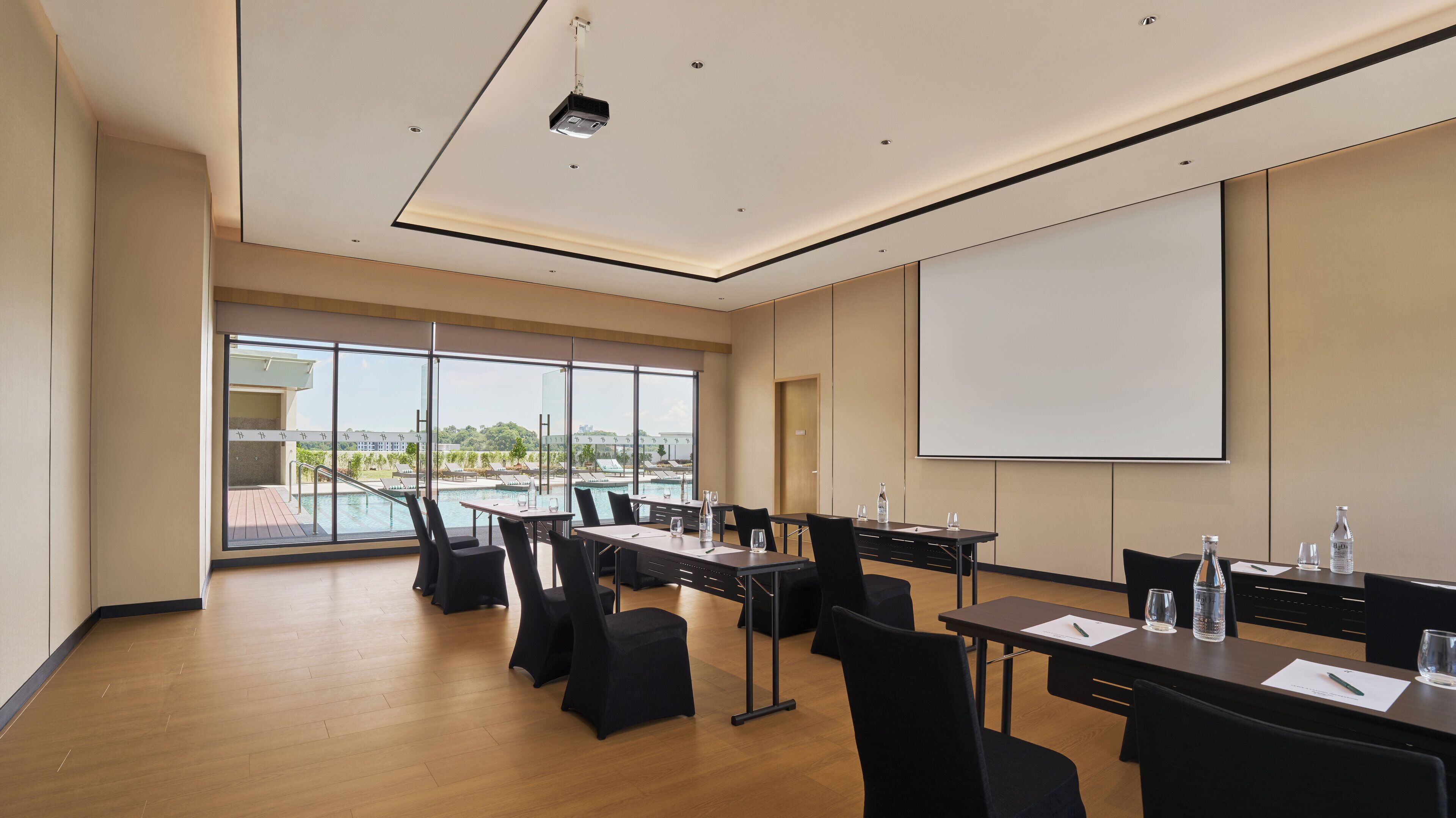 Un salón de conferencias con una pantalla grande, mesas, sillas y vista a una piscina.