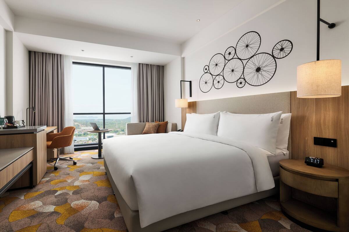 Une chambre d’hôtel avec un grand lit, un bureau avec une chaise, une petite table et une vue sur la ville.