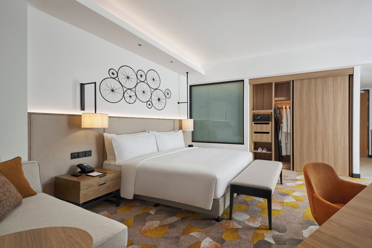 Een moderne hotelkamer met een groot bed, een bureau, een stoel, een kledingkast en een kitchenette.