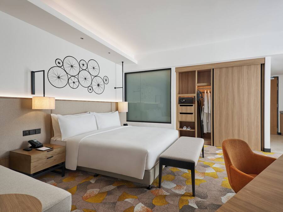Una habitación de hotel moderna con una cama grande, un escritorio, una silla, un armario y una kitchenette.