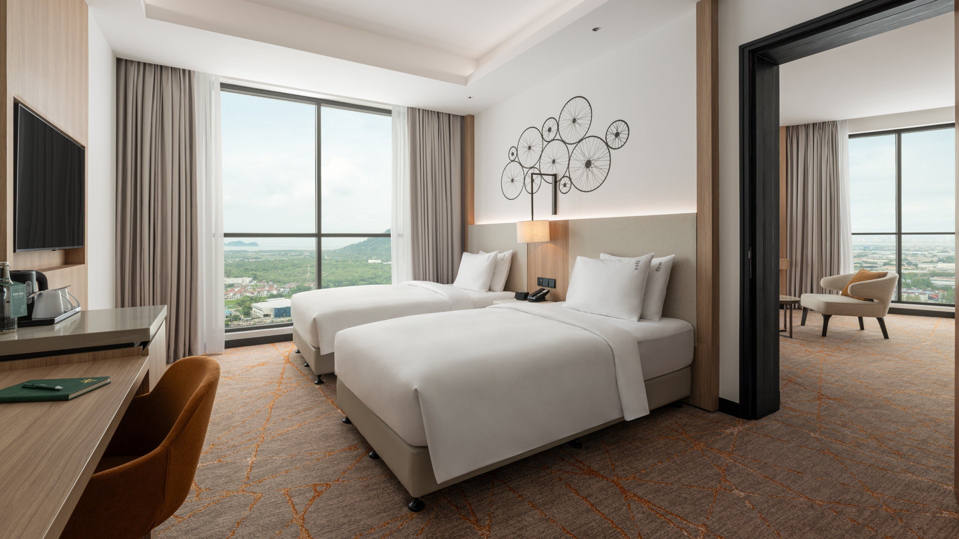 Habitación de hotel con dos camas, un escritorio con silla, televisor y un ventanal con vista a la ciudad.