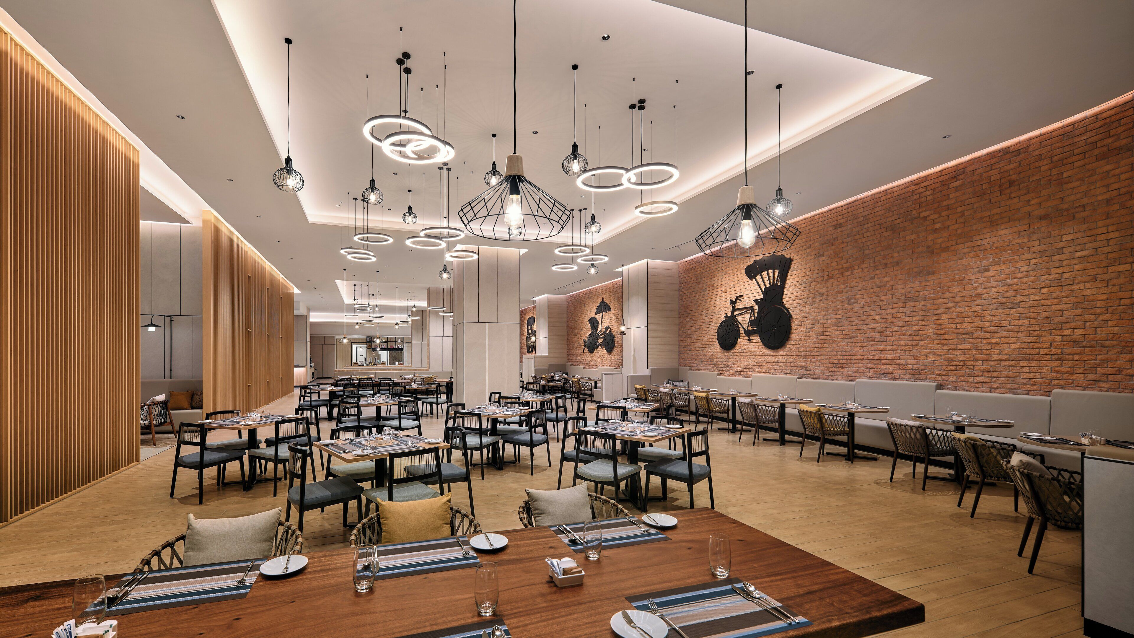 Un restaurante moderno con varias áreas de comedor, paneles de madera y un muro de ladrillo decorativo.