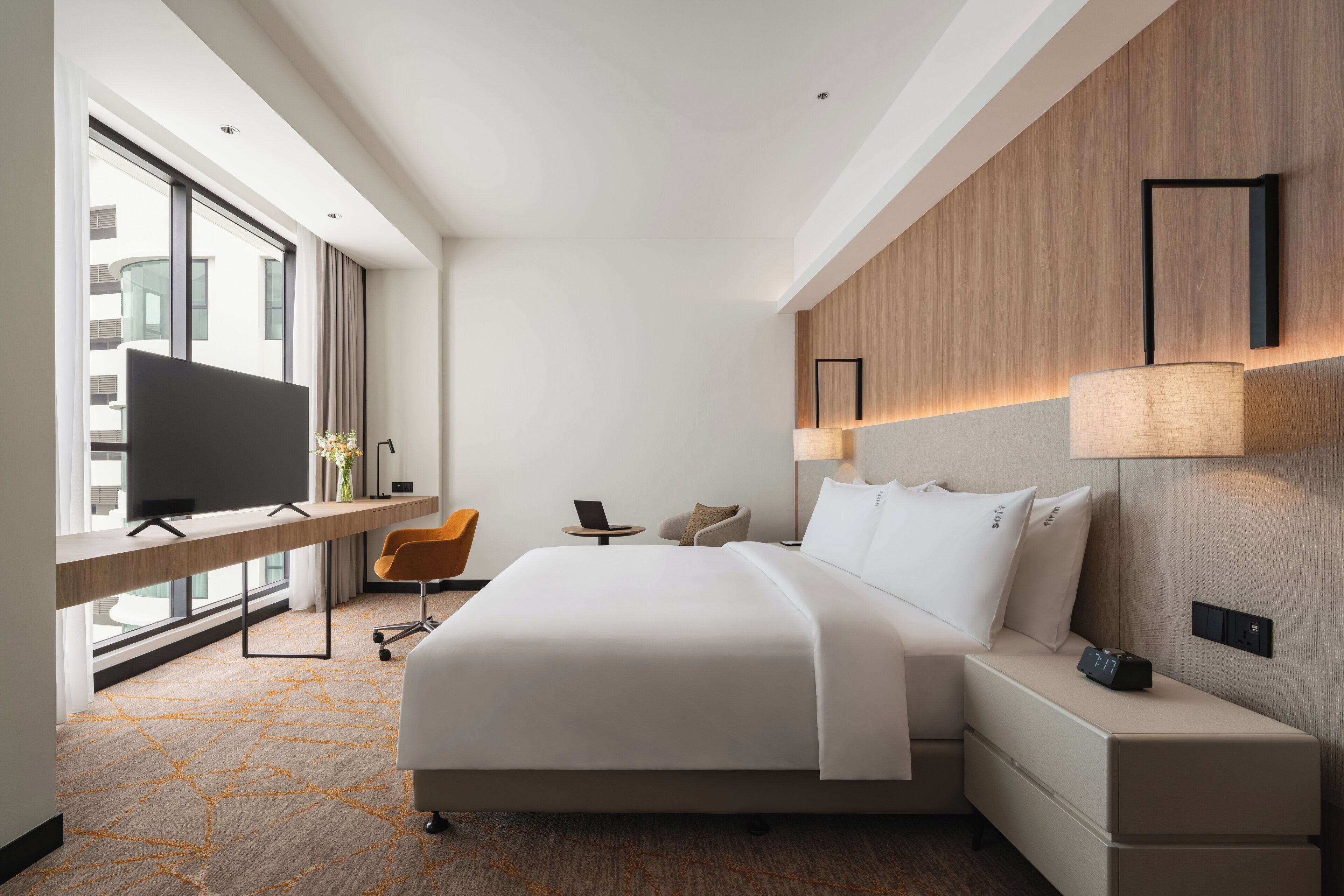 Une chambre d’hôtel moderne dotée d’un grand lit, d’un bureau avec une télévision, d’une chaise et offrant une vue sur la ville.