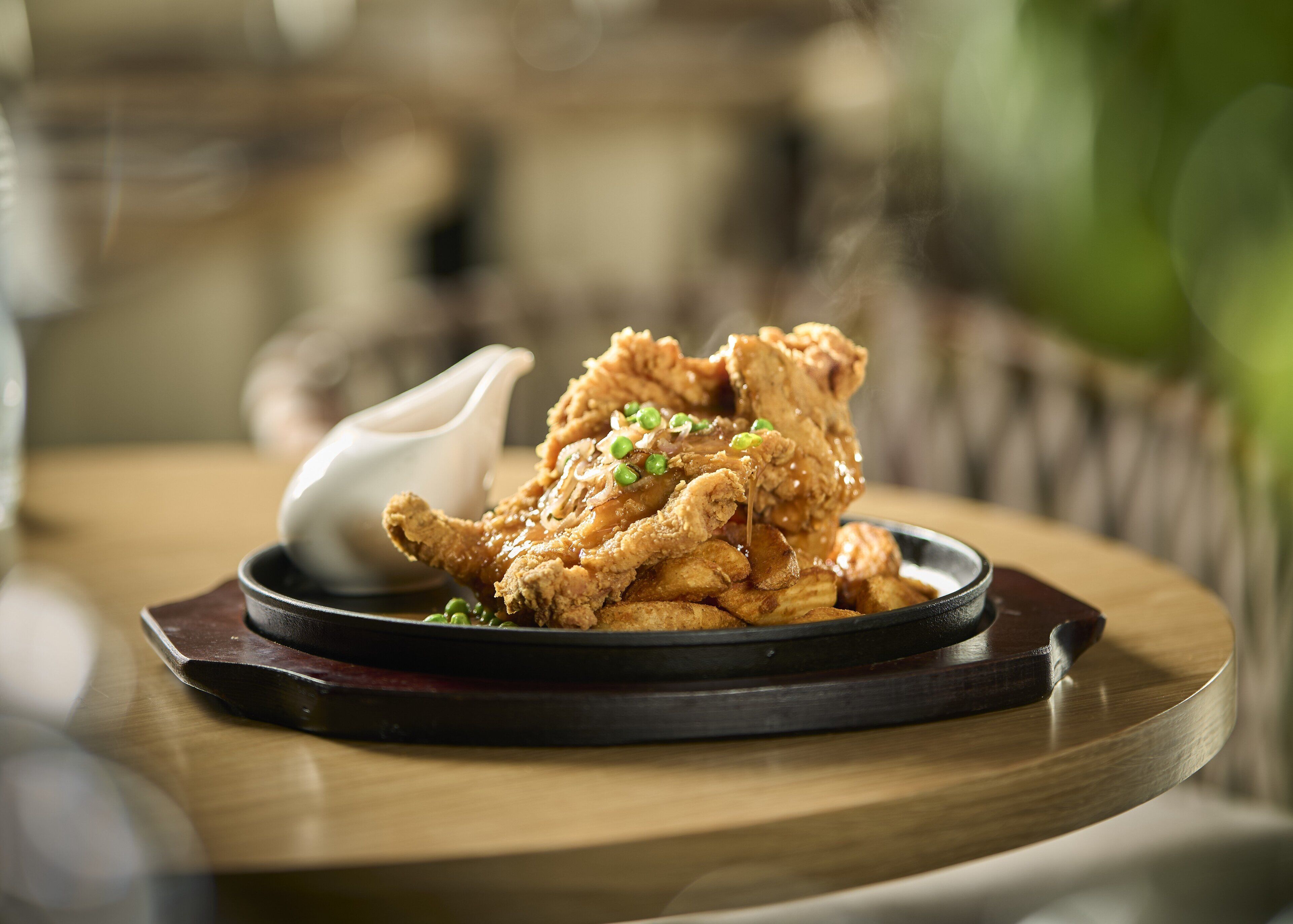 Un plato de pollo frito con salsa y cebollines sobre una mesa de madera.