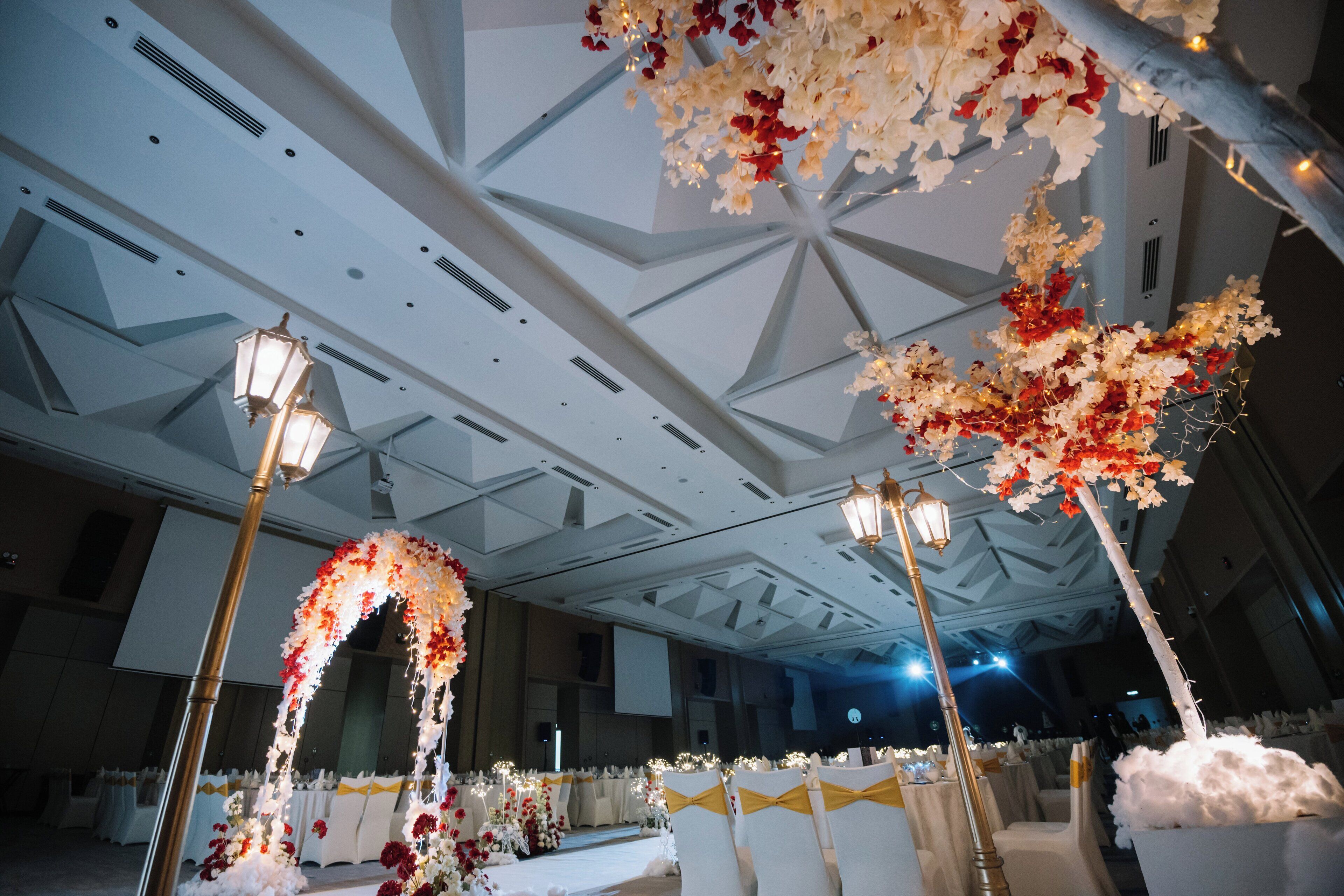 A banquet hall with a high ceiling, chandeliers, and floral decorations.