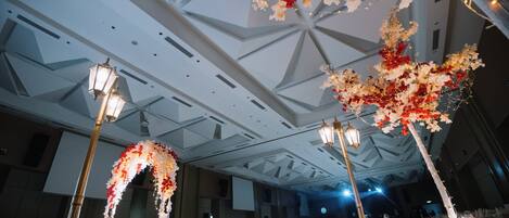 A banquet hall with a high ceiling, chandeliers, and floral decorations.