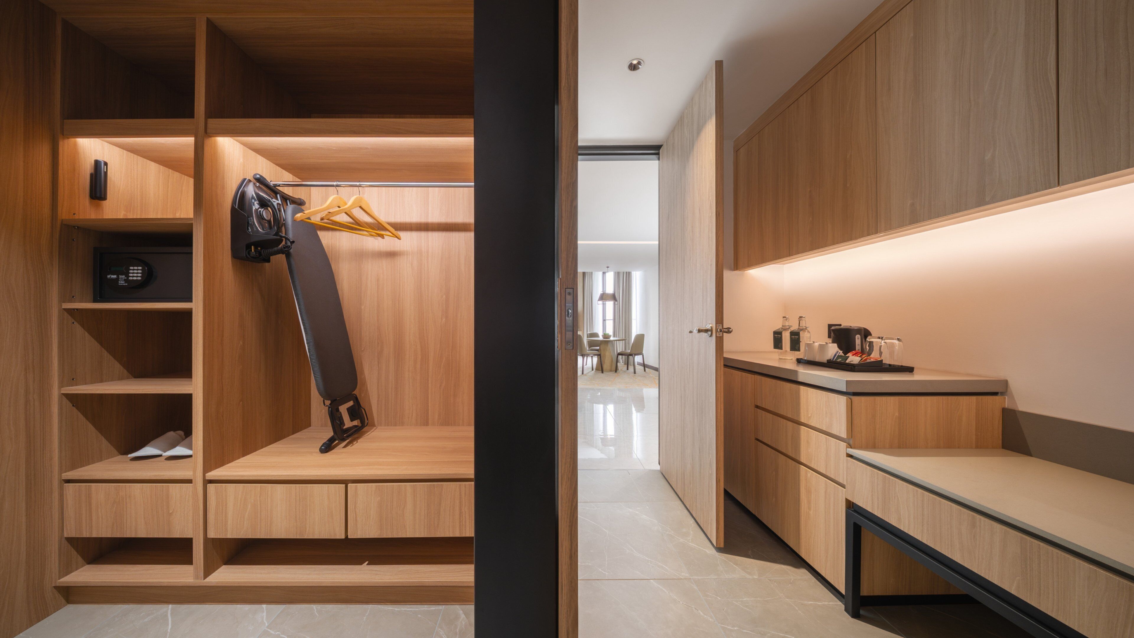 A modern hotel room with a walk-in closet, a desk with a tray of items, and a view into the adjacent room.